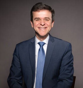 Antulio Bomfim wearing a navy blue suit jacket, white shirt, and blue tie