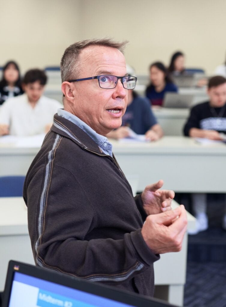 William Nelson giving a lecture, wearing a dark-colored jacket and a blue shirt