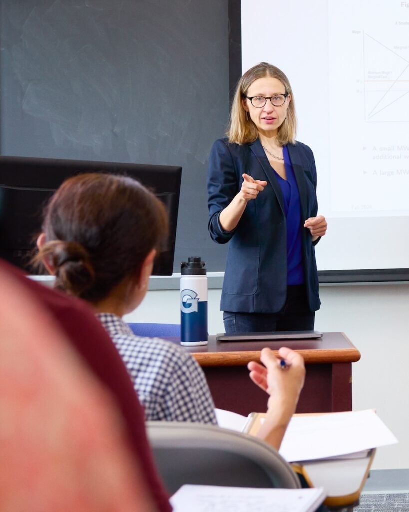 professor teaching to class in front of a chalkboard and projector